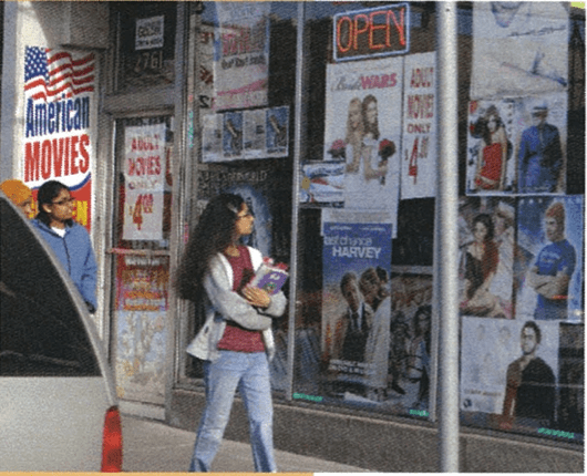 Two young women walking by a storefront while looking at the window advertisements.